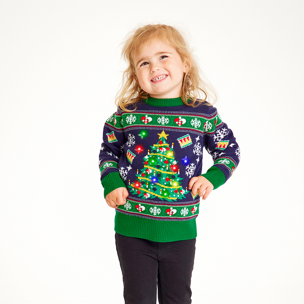 Et lille barn iført en grøn, lysende julesweater.