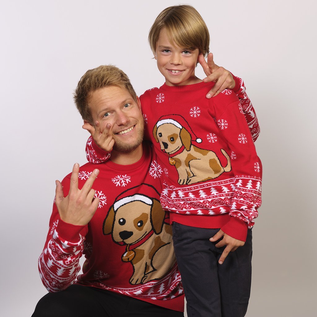 Een kind en een man dragen een rode kersttrui met een hond erop.