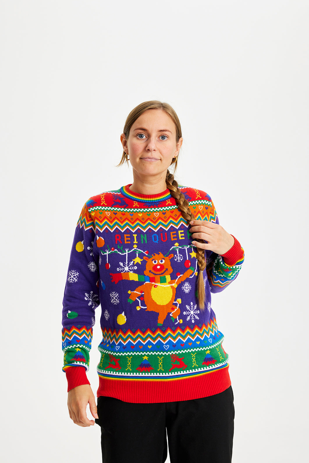 Een vrouw die een regenboogkleurige kersttrui draagt met de quote "Rein queer" erop.