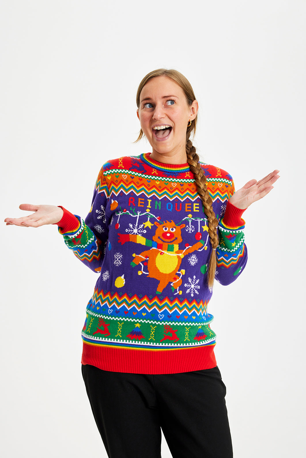 Een poserende vrouw die een regenboogkleurige kersttrui draagt met de quote "Rein queer".