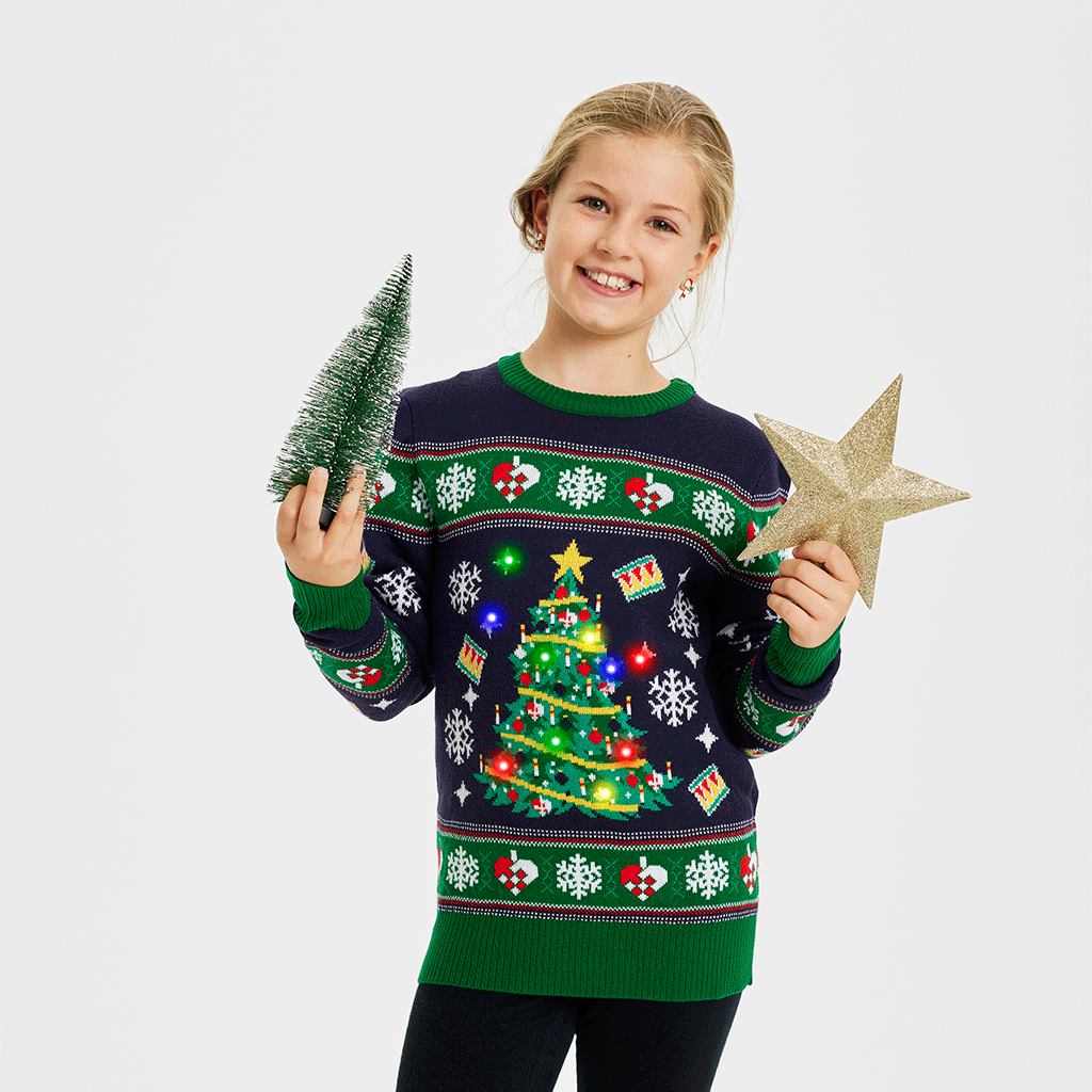 Een kind poseert in een blauwe en groene met een knipperende kerstboom.