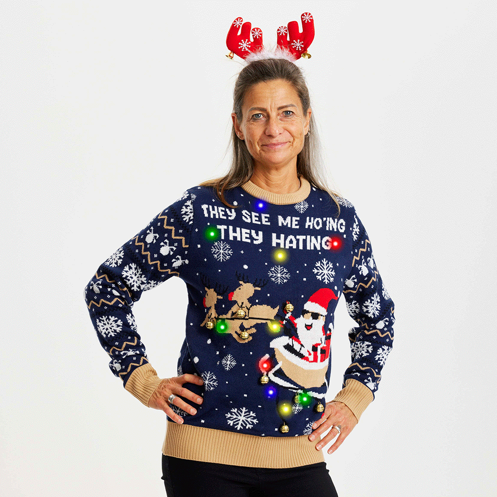 Een vrouw met haar handen langs haar zij draagt een blauwe kersttrui met de quote "They See Me Ho'ing, they hating".