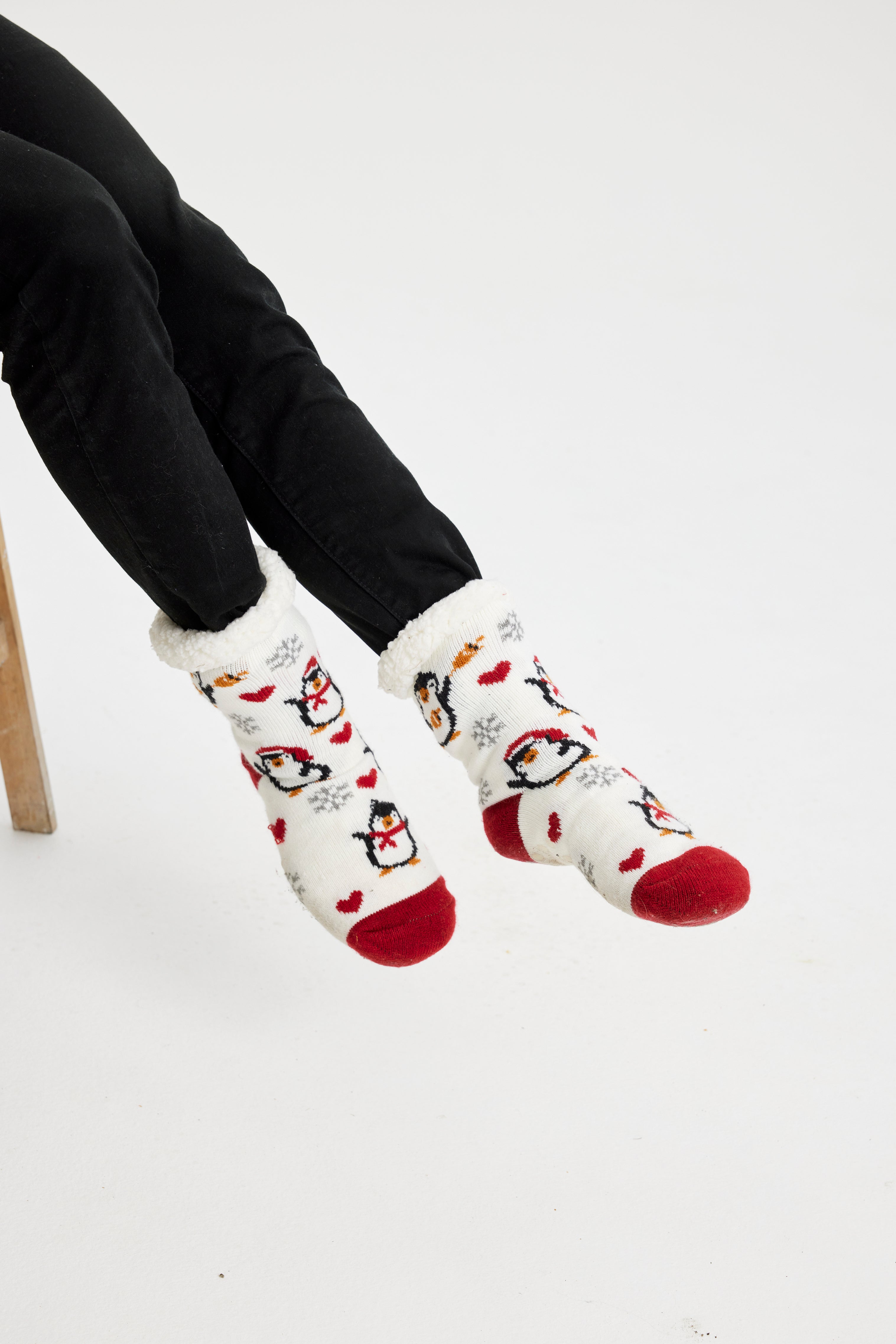 Een paar benen die witte en rode kerstsokken dragen met pinguïns erop.